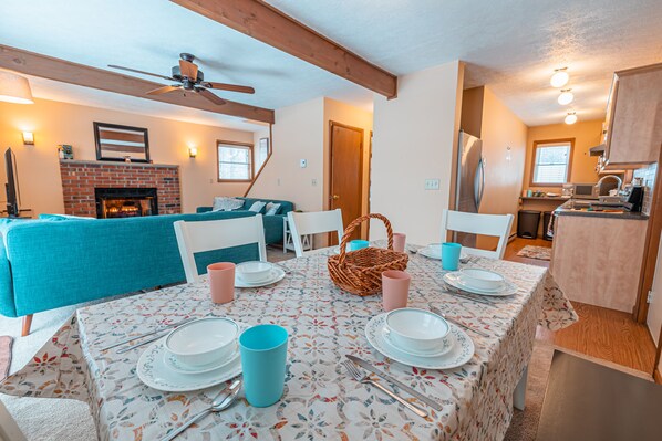 Un comedor con una mesa dispuesta para cuatro personas, una chimenea y una sala de estar con un sofá azul.