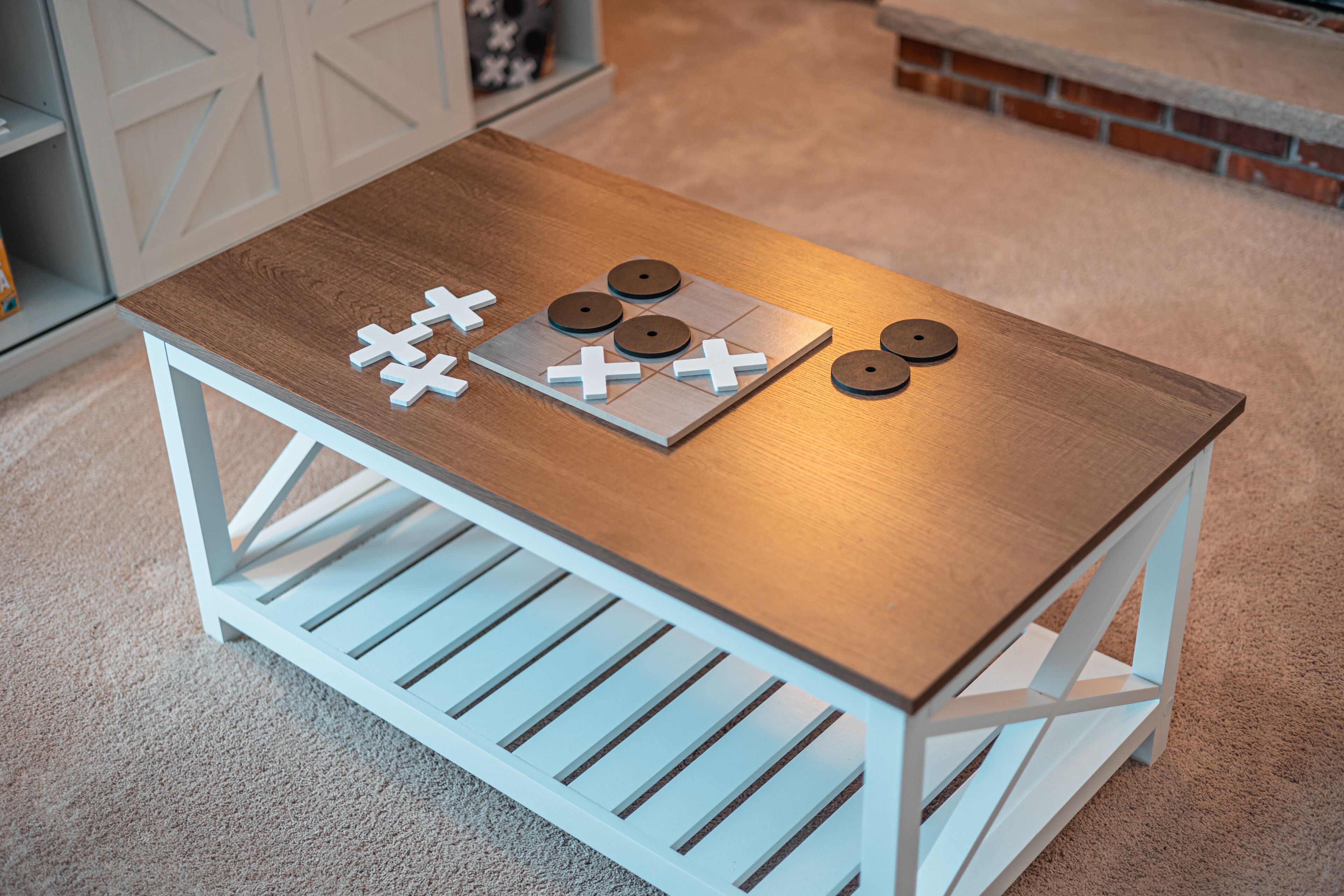 Une petite table en bois avec un cadre blanc, un plateau de jeu et des pièces de jeu, le tout posé sur un sol recouvert d’une moquette.
