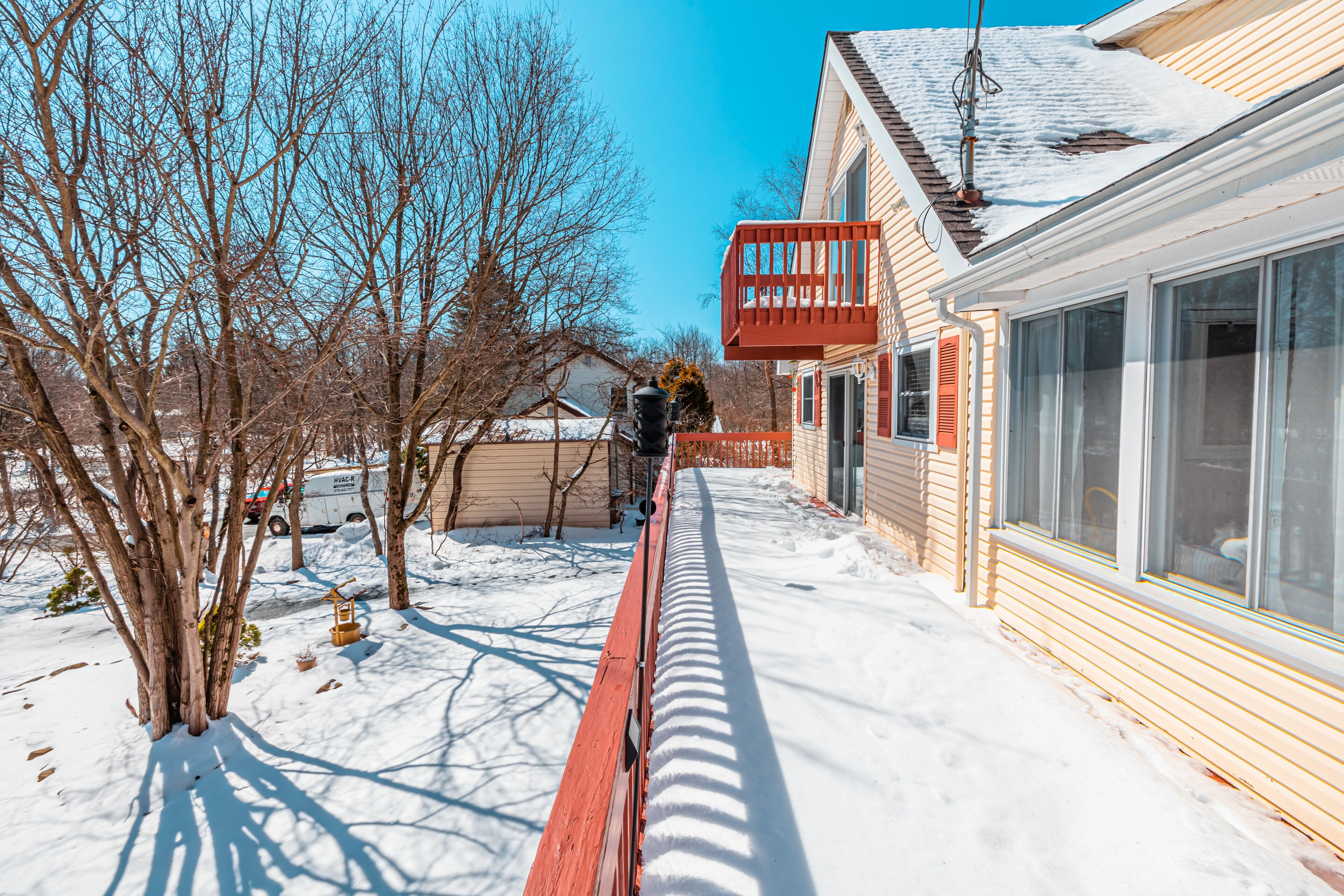 A snow-covered pathway leading to a house with a red balcony and a garage.