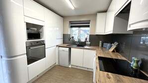 Une cuisine moderne avec des meubles blancs, un four encastré, un four à micro-ondes et un lave-vaisselle.