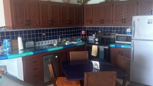 A kitchen with wooden cabinets, a blue countertop, a dining table with chairs, a ceiling fan, and a refrigerator. - Beach Front Condo with Outstanding Views  (Los Barriles)