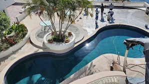 A swimming pool with a curved design, surrounded by a tiled deck and potted plants. - Beach Front Condo with Outstanding Views  (Los Barriles)