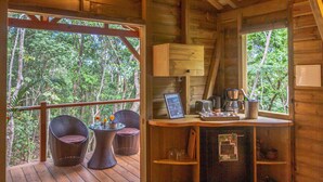 A wooden cabin with a balcony, wicker chairs, a table with drinks, a bar area, and a view of the forest. - Cabane Insolite Perchée Dans un Jardin Tropical... Le Nid des Colibris (Deshaies)