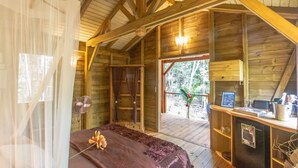 A wooden cabin with a bed, a desk, and a view of the outdoors. - Cabane Insolite Perchée Dans un Jardin Tropical... Le Nid des Colibris (Deshaies)