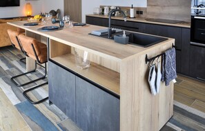 Une cuisine moderne dotée d’un plan de travail en bois, d’un évier encastré et d’un coin bar avec des tabourets.