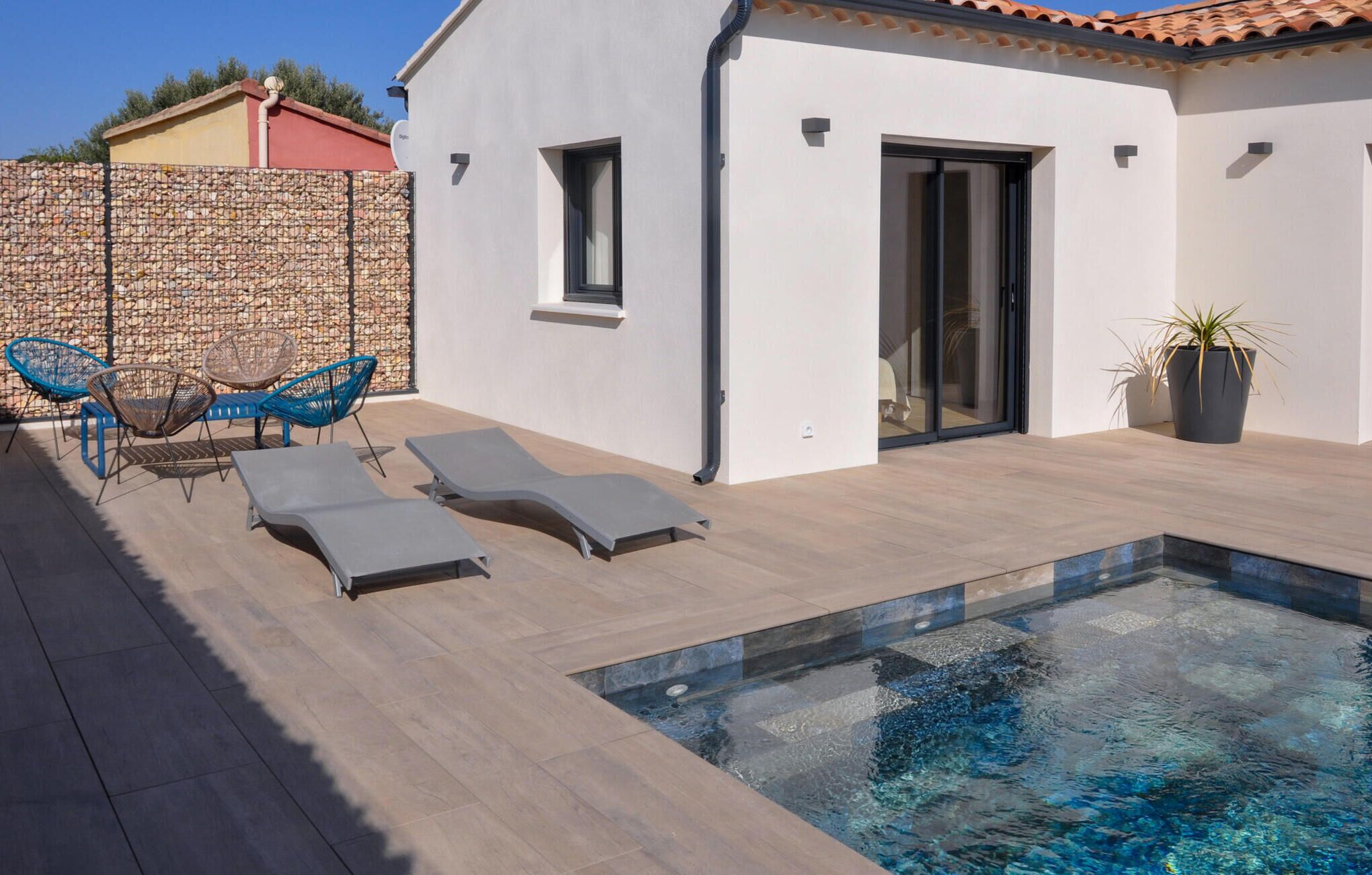 Ein moderner Poolbereich im Freien mit Liegestühlen und einer Steinmauer.