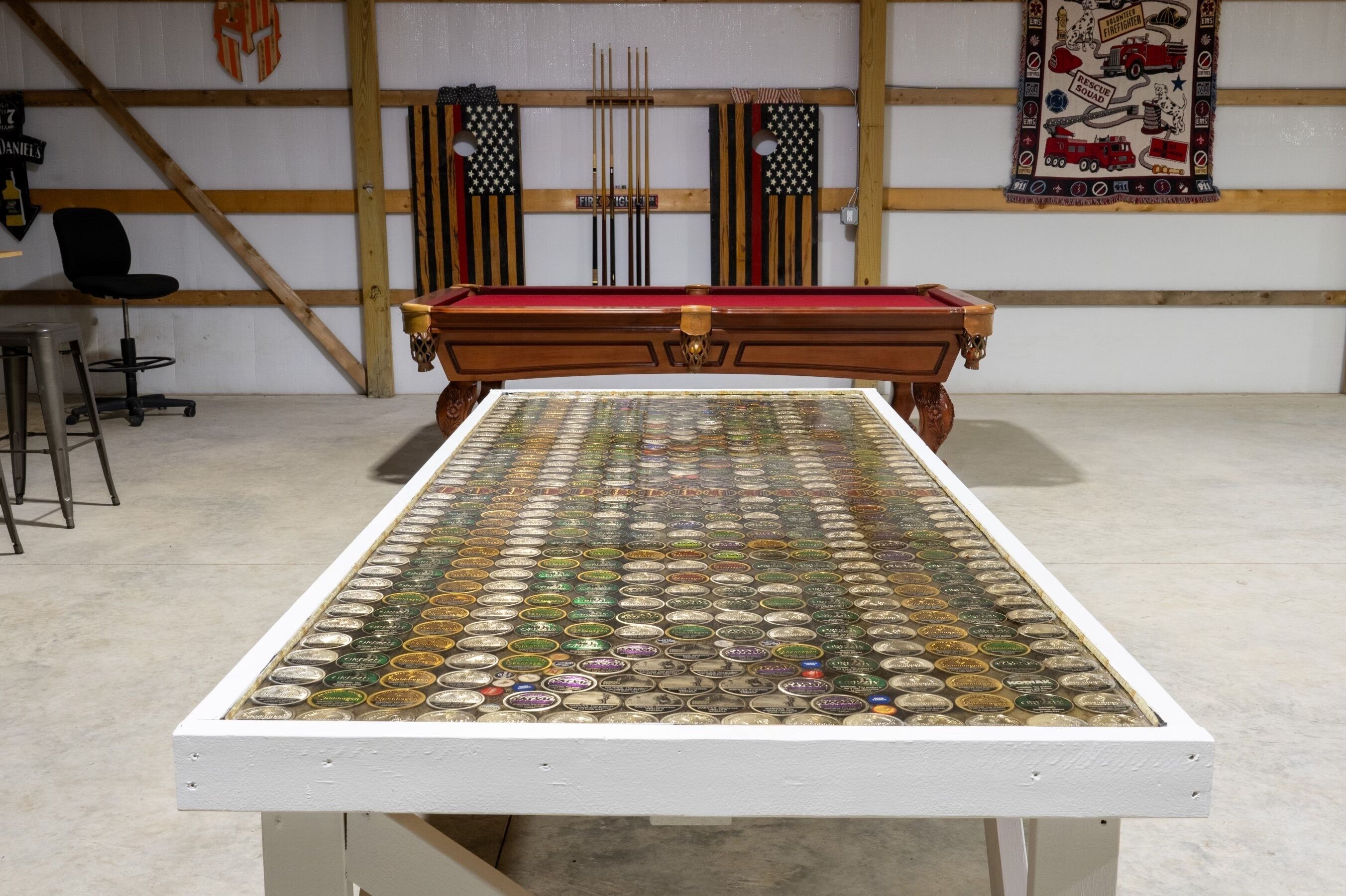 A pool table with a unique bottle cap mosaic top, a pool cue rack, and a red felt tablecloth.