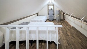 Une petite chambre mansardée étroite, avec deux lits, une commode et un radiateur.