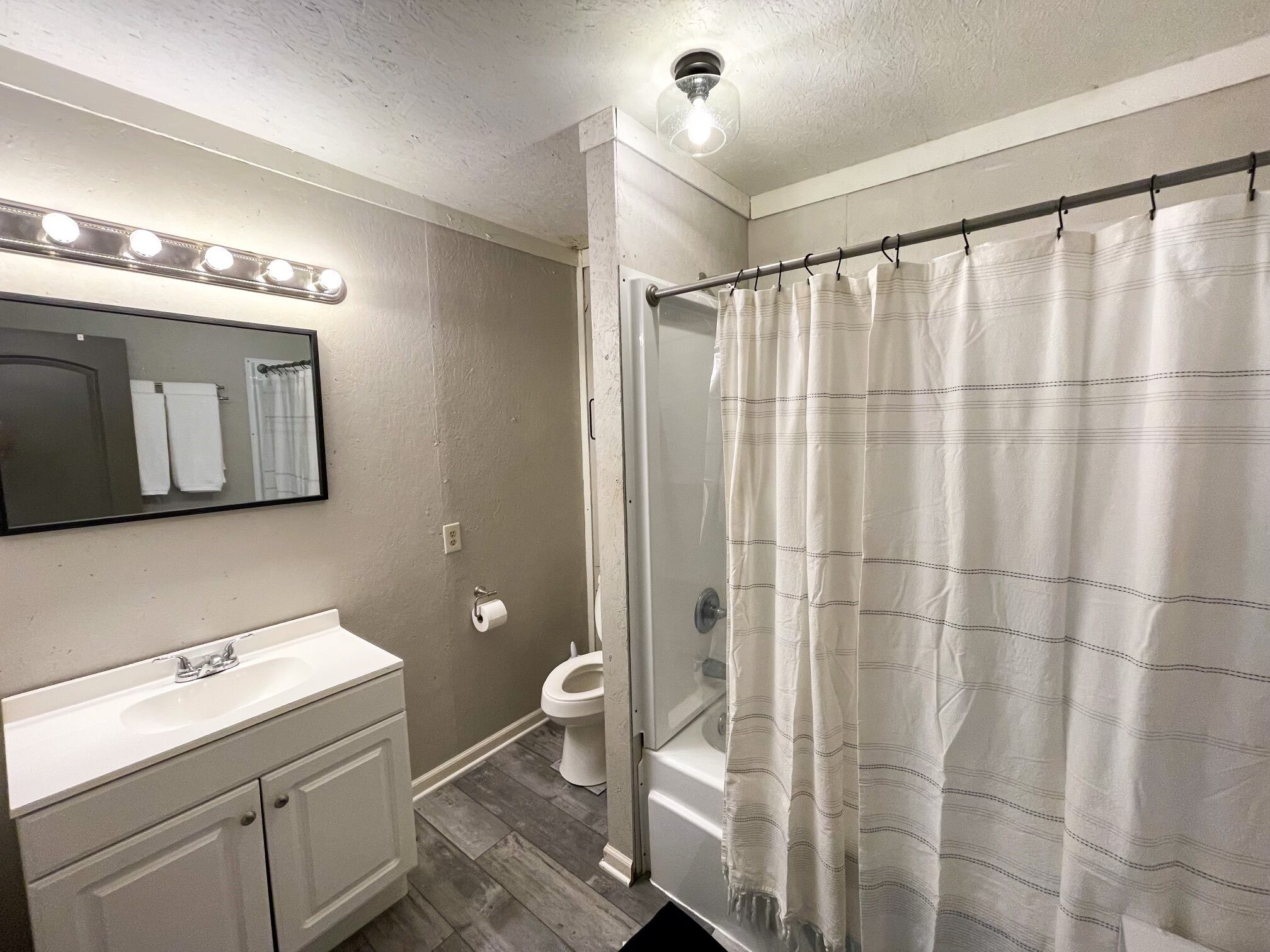 A bathroom with a vanity, a mirror, a shower curtain, and a light fixture.