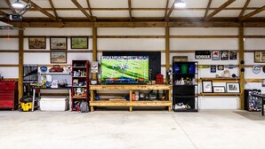 Un garage équipé d’un téléviseur diffusant un événement sportif, d’étagères en bois et de divers outils et équipements.