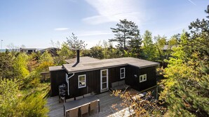 A small, dark wooden cabin with a deck, surrounded by trees and a clear sky. - 3 bedroom beautiful home in Grenaa (Grenaa)