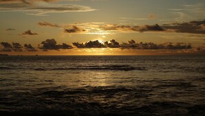 Un coucher de soleil sur l’océan, avec des nuages et une terre lointaine à l’horizon.