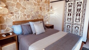A bedroom with a stone wall, a bed with a wooden frame, a nightstand, a wall-mounted air conditioner, and a decorative panel. - VERANERA, bas de villa avec vue magnifique sur le pacifique (Puntarenas Province)