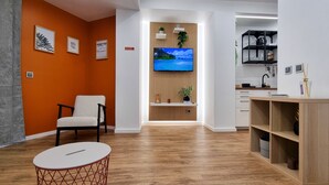 A modern living room with a wooden floor, a white round table, a beige armchair, and a TV mounted on a wooden panel wall.