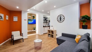 A modern living room with a grey sofa, a small round table, and a TV mounted on a wooden panel wall.