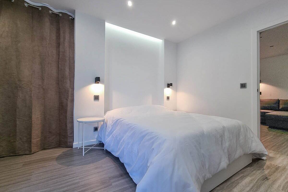 Une chambre moderne avec un grand lit, une petite table de chevet et deux lampes fixées au mur.