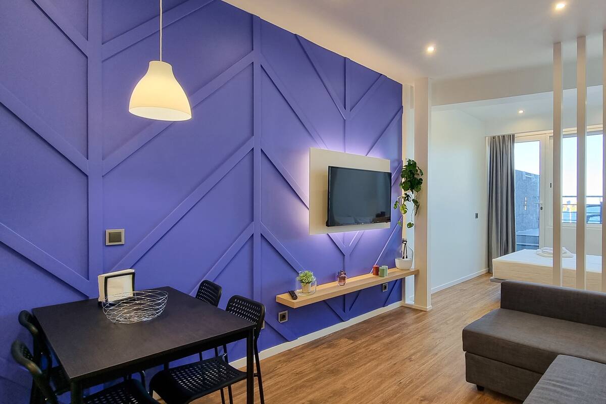 Un salon moderne doté d’un téléviseur à écran plat fixé au mur, d’un coin repas avec une table et des chaises, et d’un canapé.