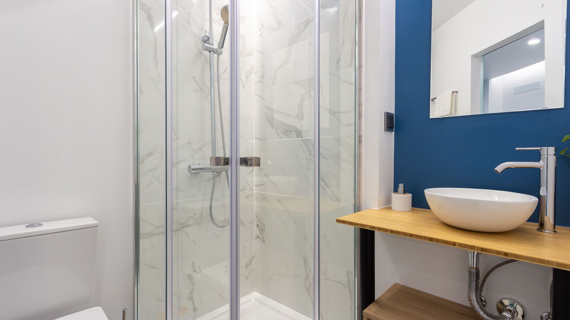 Une salle de bain moderne avec une douche à parois de verre, un lavabo blanc et un mur d’accent bleu.