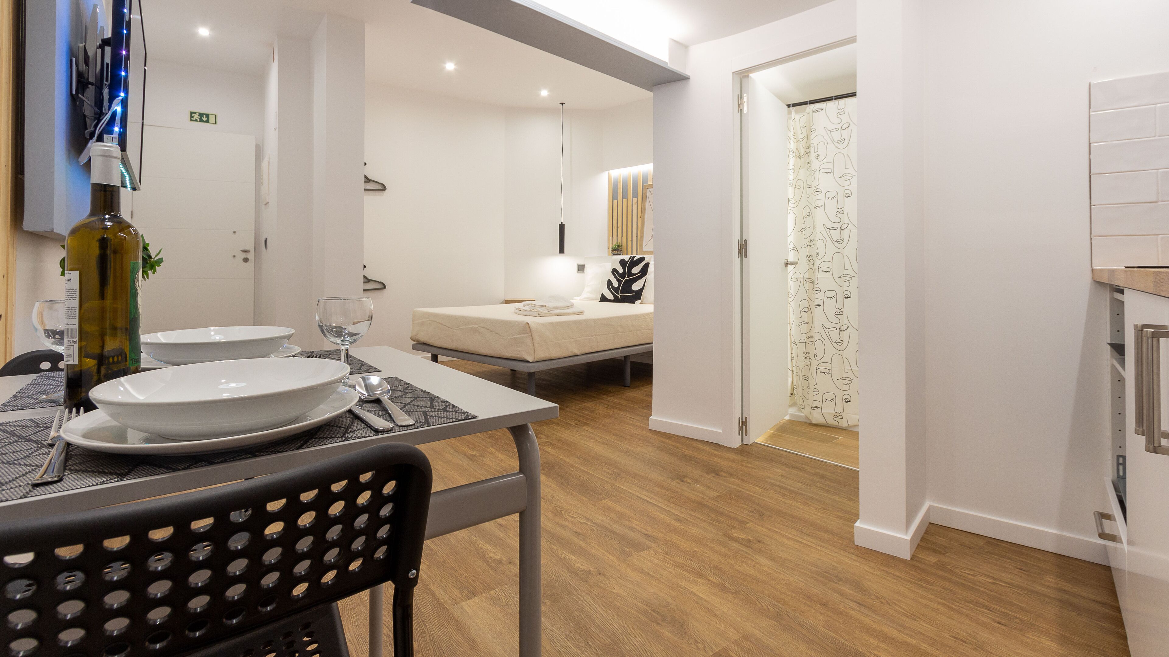 A modern hotel room with a dining area, a bed, and a shower.