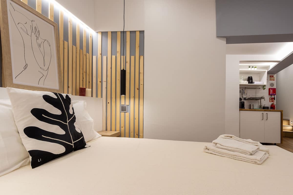 Une chambre comprenant un lit, une petite table, un coin cuisine et une œuvre d’art encadrée accrochée au mur.