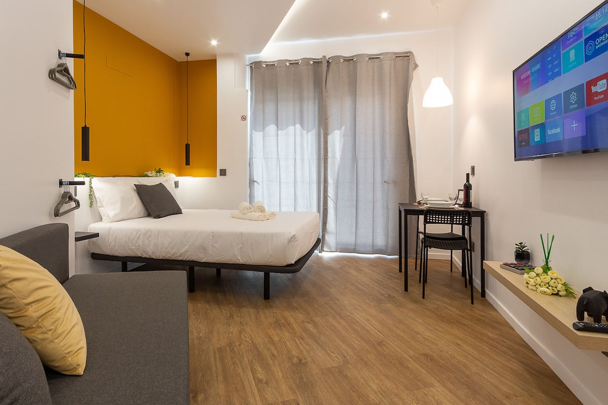 Une chambre d’hôtel moderne, équipée d’un lit, d’un canapé, d’une petite table et d’un téléviseur fixé au mur.