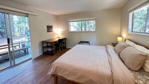 Une chambre à coucher avec un lit, un bureau et une chaise. Il y a des fenêtres et une vue sur les arbres.