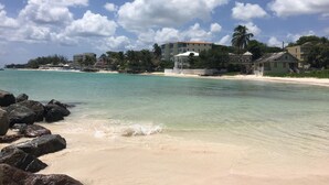Una playa con agua turquesa cristalina, una orilla arenosa y edificios al fondo.