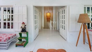 A bright, white-walled room with a wicker sofa, a green stool, and a wicker easel. - Casa Agogó - Carribean house/pool/steps from beach (Puerto Viejo de Talamanca)
