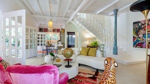 A spacious living area with a white sofa, a leopard print chair, and a globe on a coffee table. A staircase with a blue column and a colorful abstract painting is visible in the background. - Casa Agogó - Carribean house/pool/steps from beach (Puerto Viejo de Talamanca)