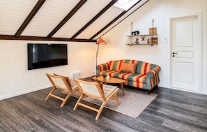 A cozy living room with a TV, a colorful striped sofa, wooden chairs, and a small table.