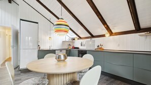 Une cuisine moderne avec une table ronde en bois, des chaises blanches et un luminaire suspendu aux couleurs vives.