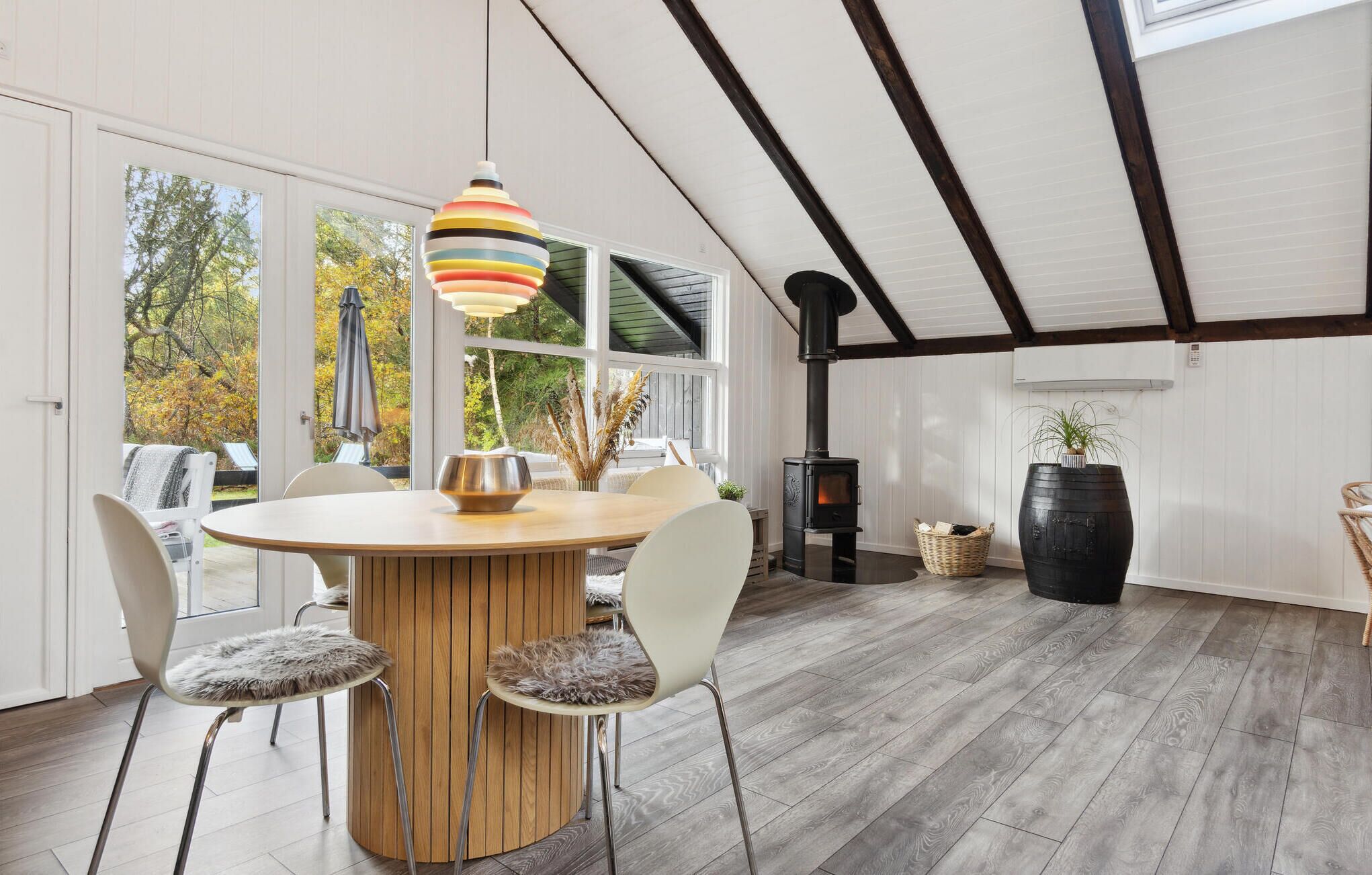 Un comedor moderno con una mesa redonda de madera, sillas blancas y una lámpara colgante de colores.