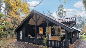 Une cabane rustique dotée d’un toit en pente, d’une terrasse en bois et d’un porche aménagé avec des sièges.