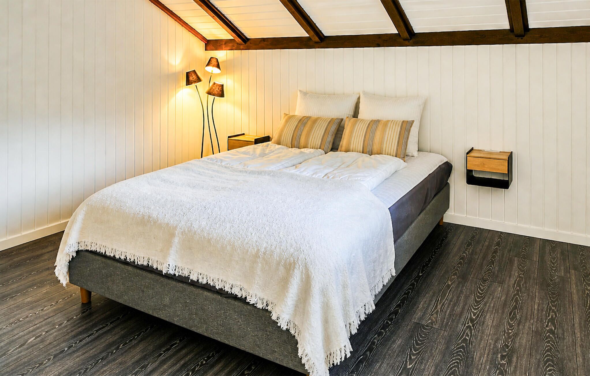 A bedroom with a bed, a nightstand, a lamp, and a wall-mounted shelf.