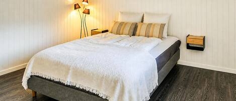 A bedroom with a bed, a nightstand, a lamp, and a wall-mounted shelf.