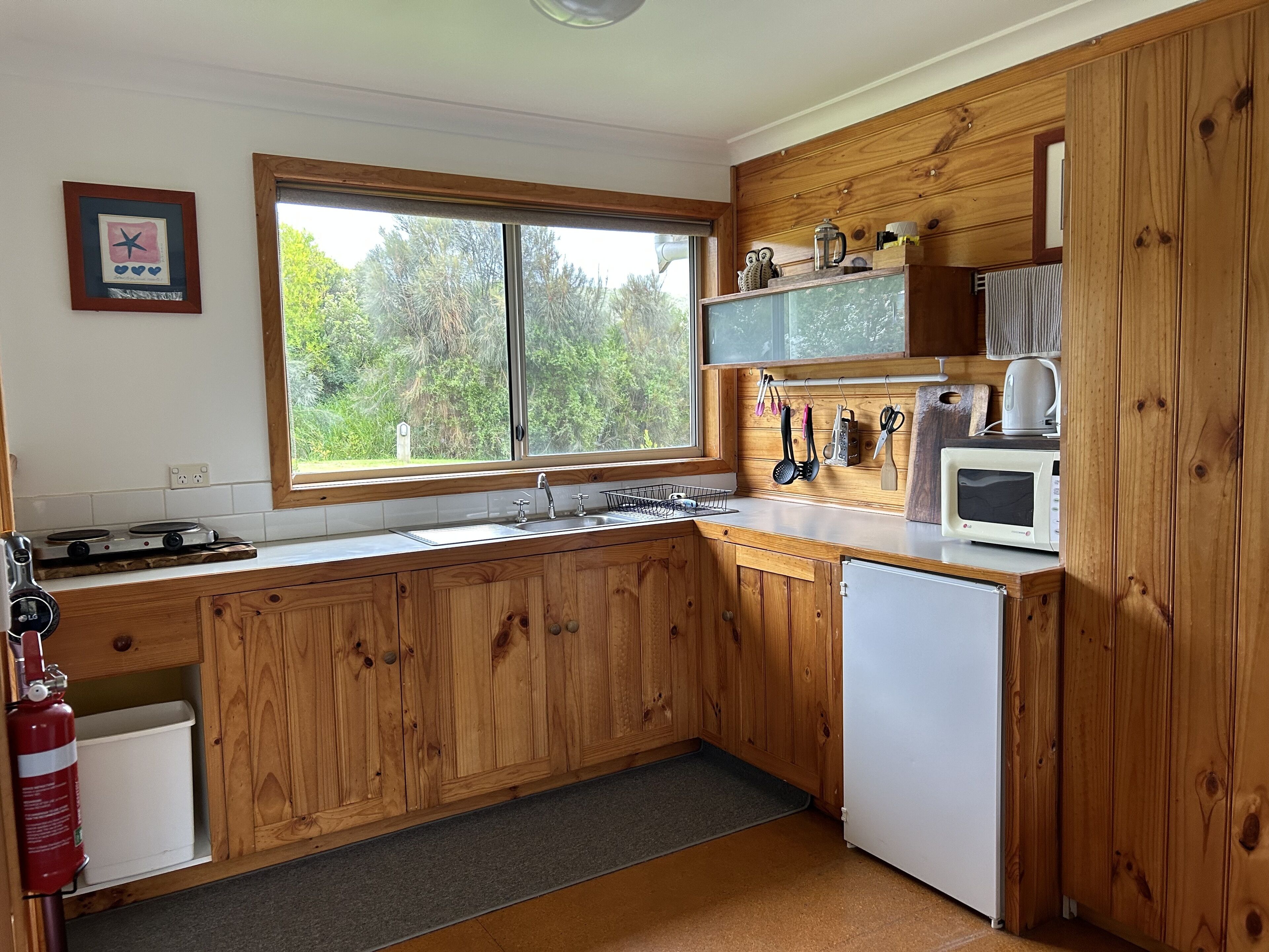 A kitchen with wooden cabinets, a window with a view of trees, a microwave, and a sink.