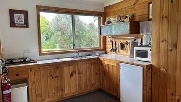 A kitchen with wooden cabinets, a window with a view of trees, a microwave, and a sink.