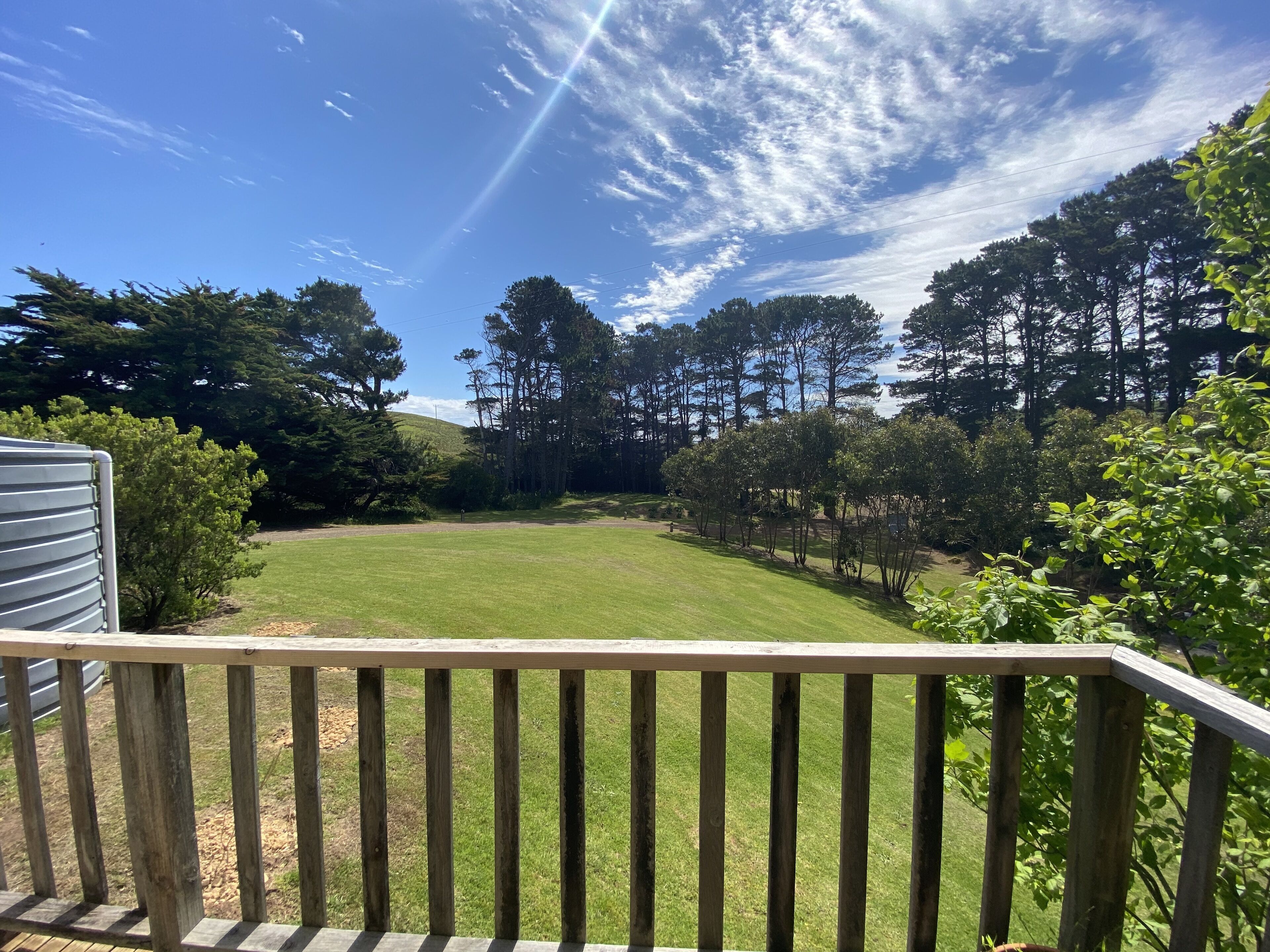 Une terrasse en bois donnant sur une pelouse bien entretenue, agrémentée d’arbres et offrant une vue sur un ciel dégagé.