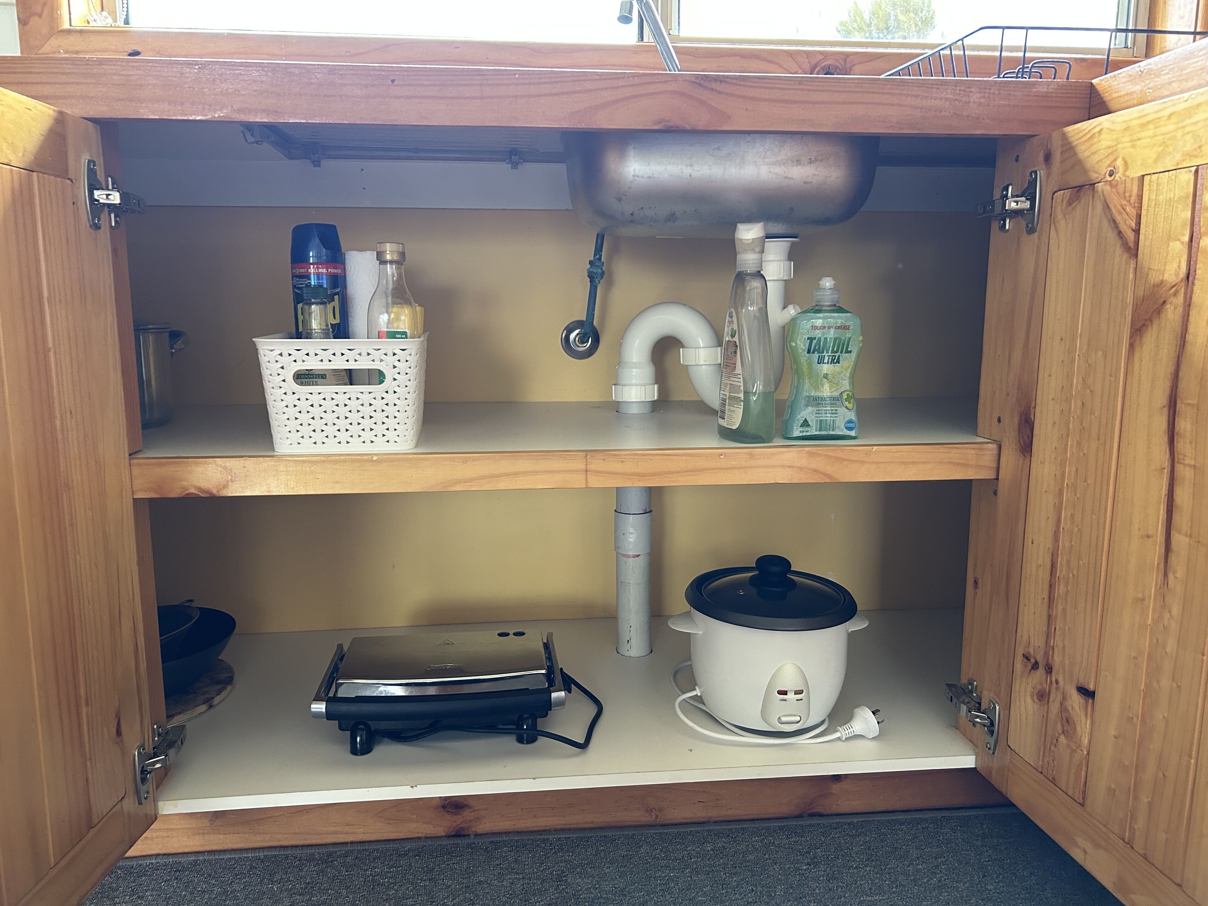 A wooden cabinet with a sink, a white basket, a bottle of hand soap, and a slow cooker.