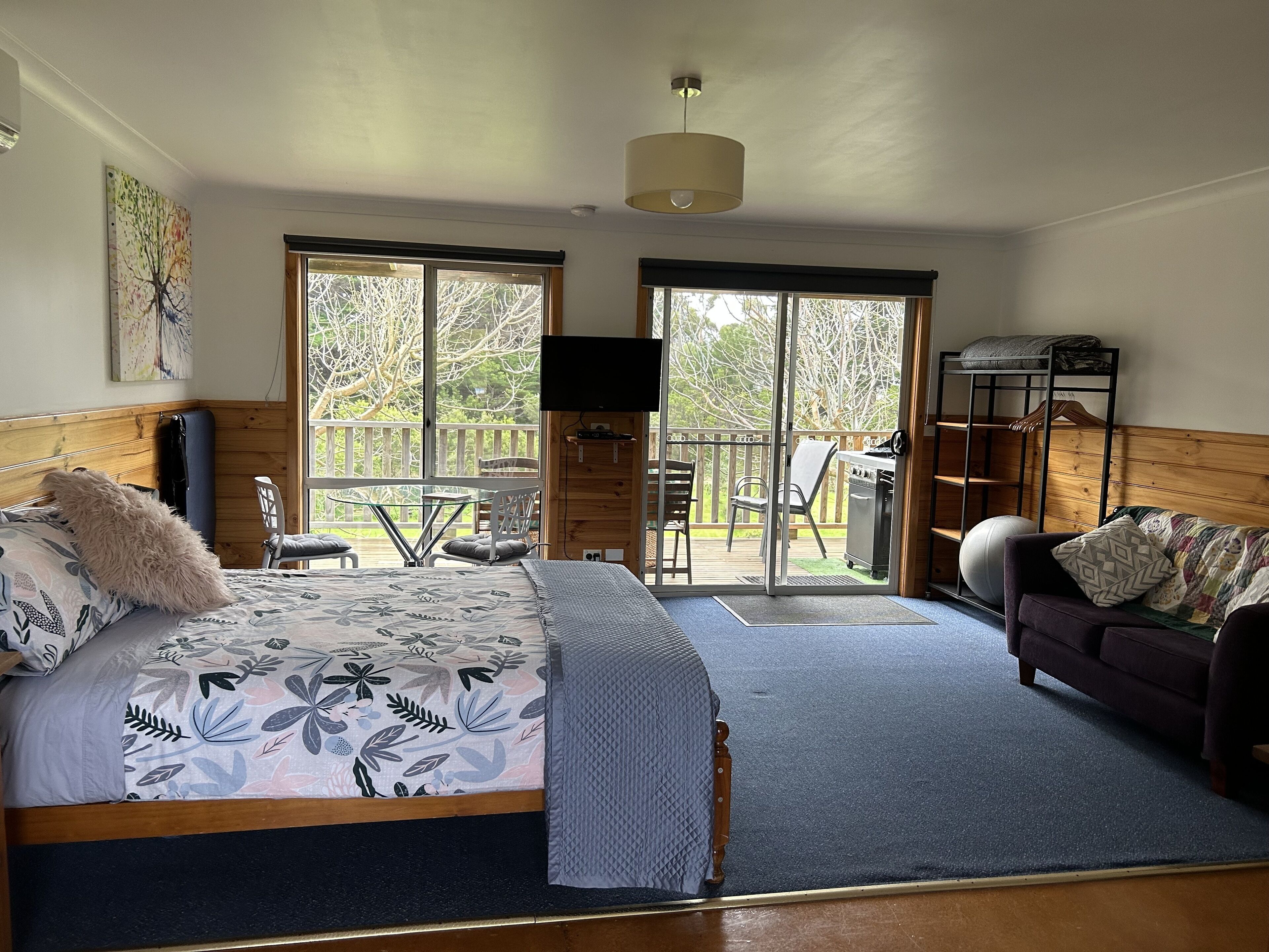 A bedroom with a bed, a sofa, a TV, and a balcony with outdoor furniture.