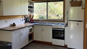 A compact kitchen with white cabinets, a built-in oven, a microwave, and a refrigerator. There's a window providing natural light and a view of greenery outside.