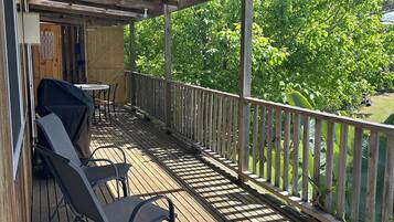 Una terraza exterior techada con suelo de madera, barandillas de metal y una parrilla.