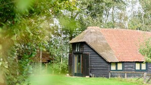 Ein rustikales Holzhaus mit einem Reetdach, umgeben von üppigem Grün.