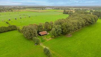 Une vue aérienne d’un paysage rural, avec des champs verdoyants, des arbres dispersés et un petit bâtiment.