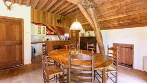 Ein rustikaler Essbereich mit Holztisch und -stühlen, einer Pendelleuchte und einer Küche im Hintergrund.