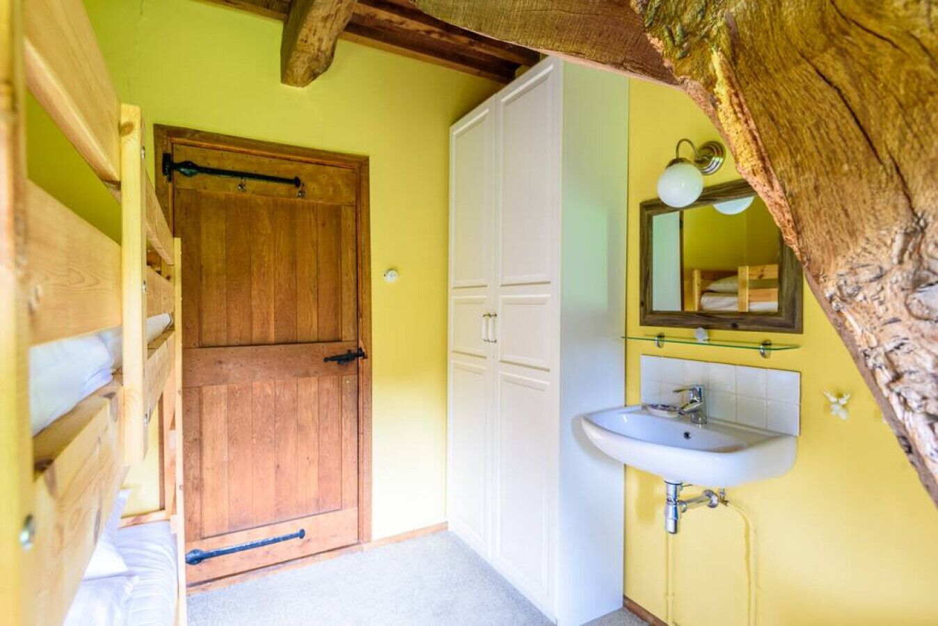 Una habitación con puerta de madera, armarios blancos, pared amarilla y un baño con lavamanos y espejo.