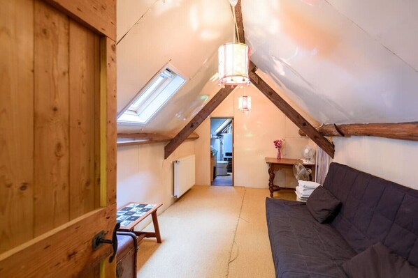 A cozy attic room with a sloped ceiling, wooden beams, a dark sofa, a small table with a board game, and a hanging light fixture. - Vrijstaand familiehuis met open haard op groot perceel | Scherpenzeel (Scherpenzeel)