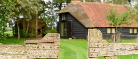 A rustic wooden gate with a metal latch, leading to a grassy area with a wooden building in the background.