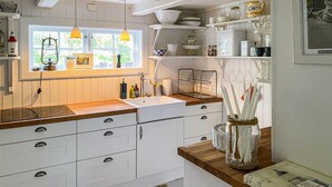 A kitchen with white cabinets, a wooden countertop, a window with curtains, hanging pendant lights, and various kitchen utensils and appliances.