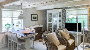 A cozy room with a dining table, wicker chairs, a cabinet, and a television.